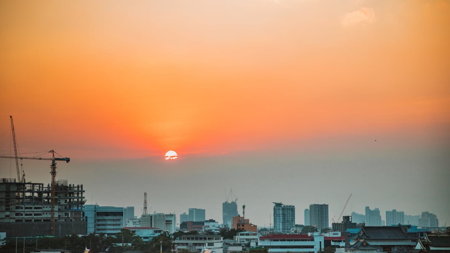 Hazy, smoke-tinted summer sky over a city skyline at sunset
